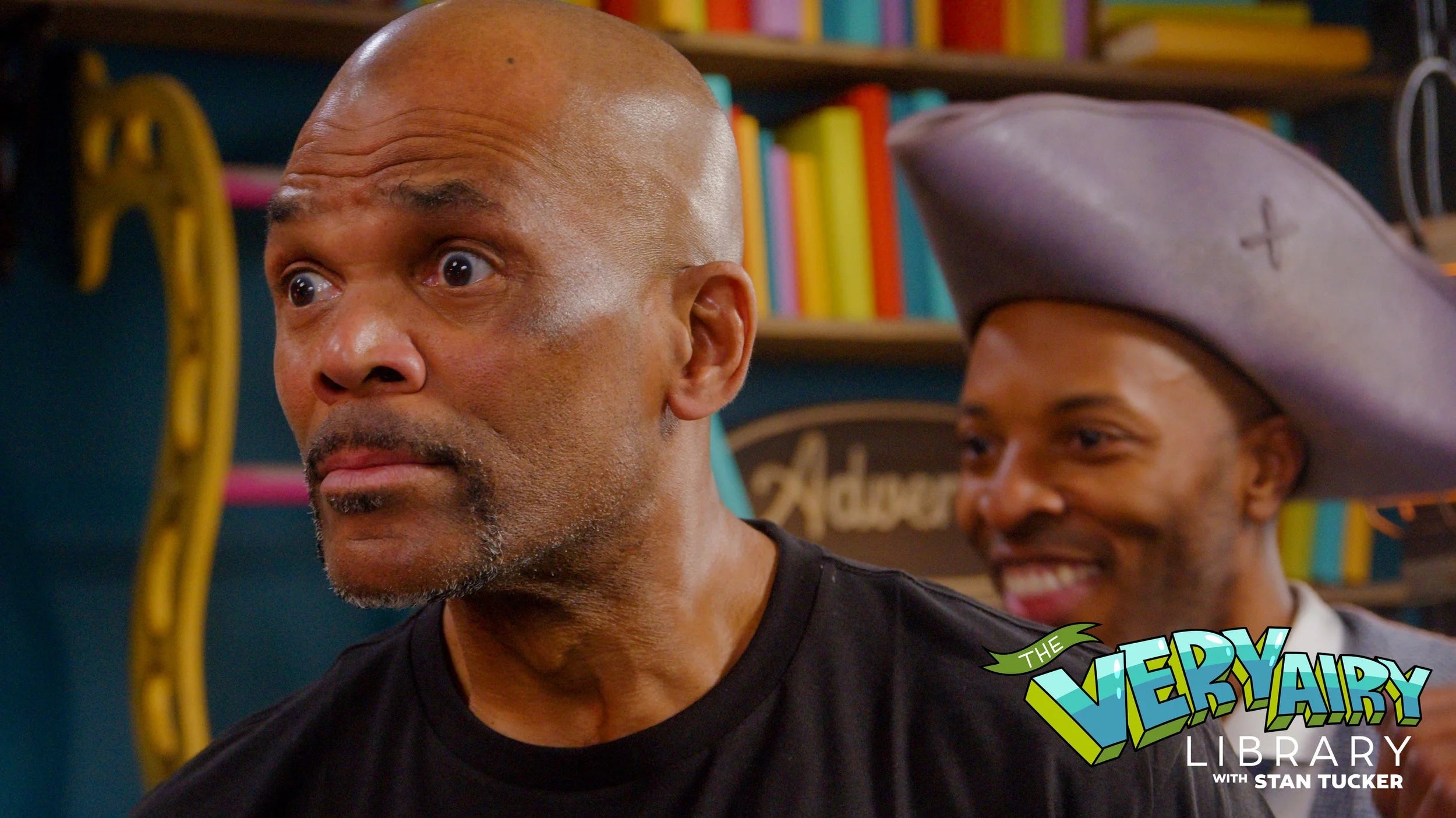 Two men in a colorful setting with 'Very Fairy Library' branding.